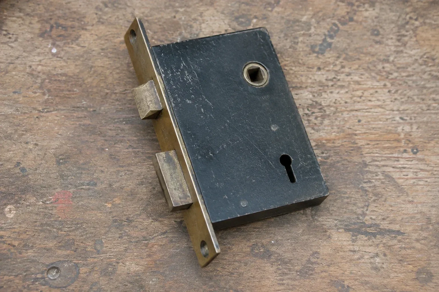 Closed mortise lock case with spindle opening, keyhole, latch and deadbolt on a wooden workbench. — Vintage Mortise Lock Service, Oro-Medonte