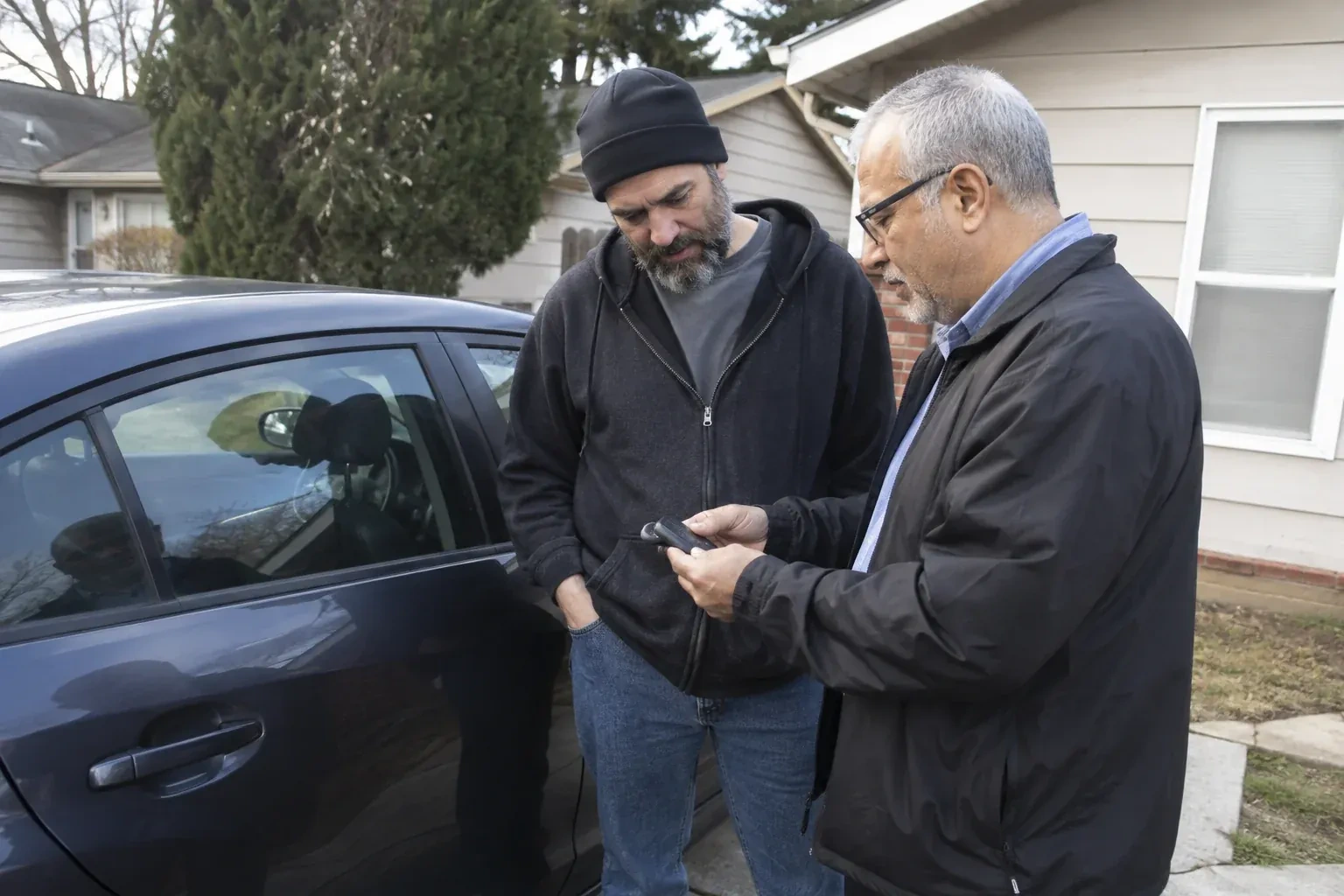 Two adults discussing a key fob beside a parked car. — Car Lockout Service, Oro-Medonte